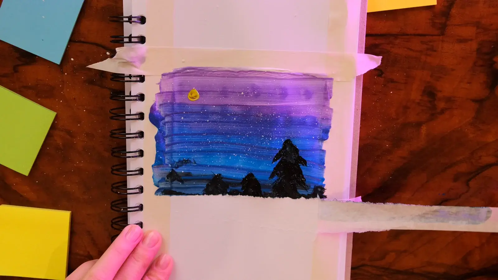 Hands working on a masked acrylic landscape painting from the Creative Hands sample